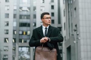 comprobando la hora. hombre de negocios con traje negro y corbata está al aire libre en la ciudad foto