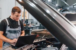 Using laptop. Man in uniform is working in the auto service photo