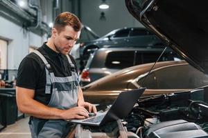 Using laptop. Man in uniform is working in the auto service photo