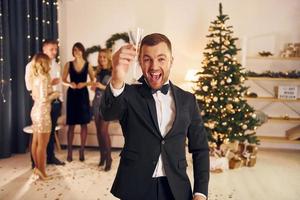 Man with glass of champagne is cheering. Group of people have a new year party indoors together photo