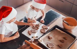 en sombreros de santa. niño y niña preparando galletas navideñas en la cocina foto
