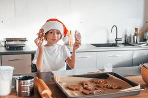 niña pequeña preparando galletas navideñas en la cocina foto