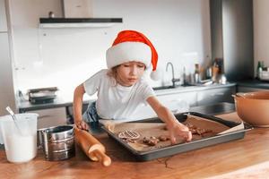 niña pequeña preparando galletas navideñas en la cocina foto