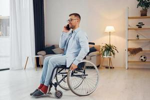 usando el teléfono hombre discapacitado en silla de ruedas está en casa foto