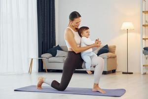 Standing on the mat and doing exerises. Mother with her little daughter is at home together photo