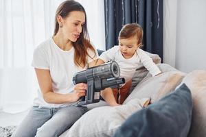 Little part of the vacuum cleaner. Mother with her little daughter is indoors at home together photo