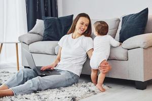 portátil de color plateado. madre con su pequeña hija está adentro en casa juntos foto