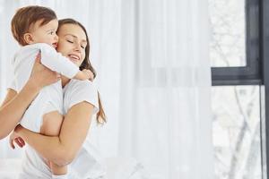 abrazándose unos a otros. madre con su pequeña hija está adentro en casa juntos foto