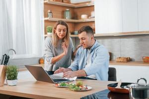 Using internet. Couple preparing food at home on the modern kitchen photo