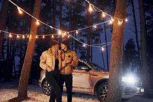 automóvil estacionado detrás. pareja de pie en el bosque y celebrando el año nuevo foto