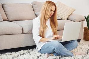 trabajando desde casa. mujer joven en camisa blanca y jeans en el interior foto