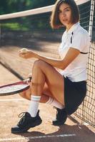 Sitting and holding racket. Female tennis player is on the court at daytime photo