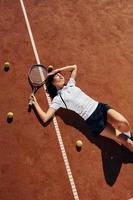 Laying down on the ground. Female tennis player is on the court at daytime photo