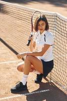 Sitting and posing. Female tennis player is on the court at daytime photo