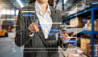 el trabajador de almacenamiento en uniforme con casco comprueba las existencias y el inventario y el diagrama de programación del diagrama de Gantt. negocios con una tableta en el almacén foto