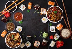 Traditional Japanese food - sushi, rolls, rice with shrimp and udon noodles with chicken and mushrooms on a dark background. Top view photo