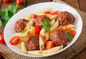 Penne pasta with meatballs in tomato sauce in a white bowl photo