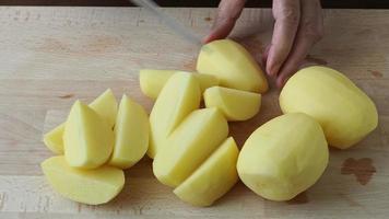 mãos com uma faca cortando as batatas na tábua de madeira da cozinha. alimentação saudável e estilo de vida. video