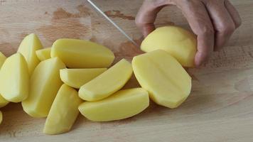 main de femme avec un couteau coupant les pommes de terre sur la planche de bois dans la cuisine. une alimentation et un mode de vie sains. video