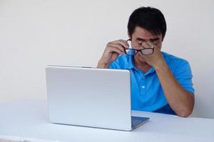 Asian man, feels hurt his eyes, holds eyeglasses during working on laptop. concept , Eyesight problem. Optometry. Glasses with convex or concave lenses. Myopia.Eye disease photo