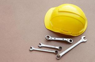 Yellow helmet and wrenches on brown background. Concept, handyman or mechanic tools. Equipment for fixing or repairing, renovation in daily life. photo