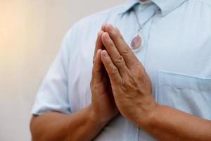 Closeup man in blue shirt ,wears Buddha amulet, praying with hands buddhist pray gesture, Wai in Thai culture. Concept, woreship for lucky, faith and belief. Pattern of respect and greeting. photo