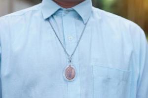 Closeup man in blue shirt wear Thai Buddha amulet necklace. Concept, faith and belief of Buddhist for holy to protect from dangers, bring good luck, business prosperity and wealth. photo