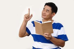 Handsome Asian man holds book and point index finger up. Concept, reading book, get knowledge and idea. Preparing for test. Education. Hobby and pastime. Read for pleasure. Copy space for add text. photo