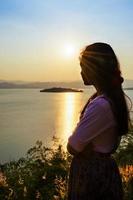 mujer joven feliz de pie viendo la puesta de sol sobre el lago foto