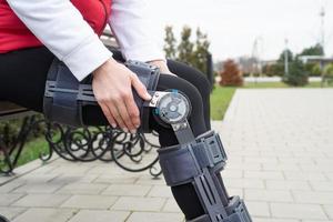 Woman wearing knee brace or orthosis after leg surgery, walking in the park photo