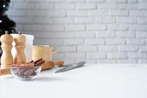 mesa de cocina con herramientas para hornear, canela y árbol de navidad en el fondo foto