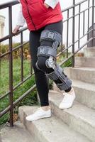 Woman wearing knee brace or orthosis after leg surgery, walking in the park photo