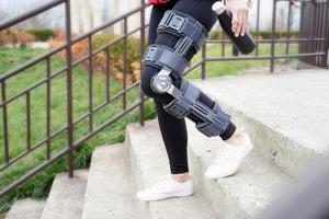 Woman wearing knee brace or orthosis after leg surgery, walking in the park photo