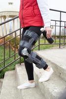 Woman wearing knee brace or orthosis after leg surgery, walking in the park photo