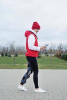 Woman wearing knee brace or orthosis after leg surgery walking in the park using smartphone photo