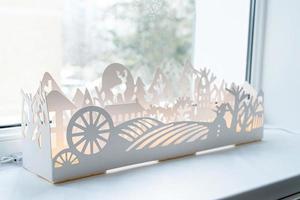 Beautiful white paper or plastic winter decoration with lights on windowsill photo