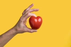 la mano sostiene un tomate rojo en forma de corazón, símbolo de amor, sobre un fondo amarillo. concepto de comida saludable. día de San Valentín. foto