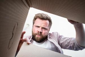 el hombre desempacó la caja entregada con el paquete, frunce el ceño y se enoja, no le trajeron lo que ordenó. Vista interior del desempaquetado. foto