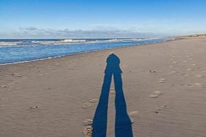 Image of a long shadow of a person on a wide sandy beach photo