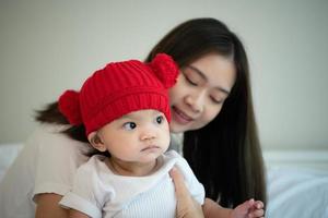 madre y bebé recién nacido con sombreros rojos en el dormitorio blanco, luz solar cálida en la noche del día foto