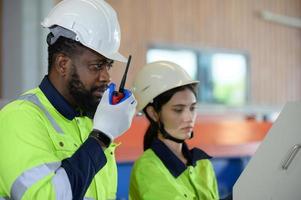 joven ingeniera aprendiendo a operar maquinaria en una fábrica con ingenieros veteranos foto