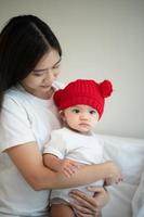 madre y bebé recién nacido con sombreros rojos en el dormitorio blanco, luz solar cálida en la noche del día foto