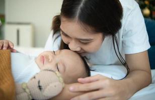 Young mother hugging her newborn child to lull the baby to sleep in the white bedroom photo