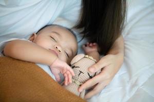 Young mother hugging her newborn child to lull the baby to sleep in the white bedroom photo