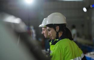 joven ingeniera aprendiendo a operar maquinaria en una fábrica con ingenieros veteranos foto