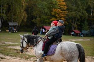 Two children are sitting on a horse, happy children are walking in the forest with a horse. photo