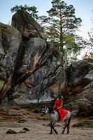 Dovbush rocks and horse riding, a woman riding a horse in a red dress with bare feet. photo