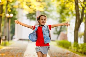 The little schoolgirl is running with a backpack and laughing. The concept of school, study, education, friendship, childhood. photo