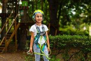 Portrait of little smiling girl in helmet and harness on trail in sky rope park in summer. photo