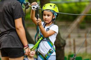 Niña de la escuela feliz disfrutando de la actividad en un parque de aventura de escalada en un día de verano foto